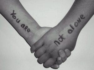 Two hands holding each other, one hand says "You are" on the wrist and the other says "not alone", to read "You are not alone"